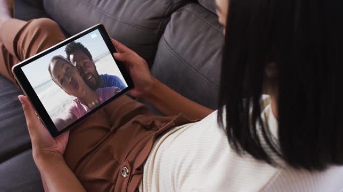 非裔美国妇女坐在家里的沙发上在数字平板电脑上进行视频通话