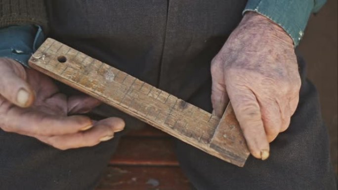 一个老人的手拿着一个木制的角度，并指示刻度