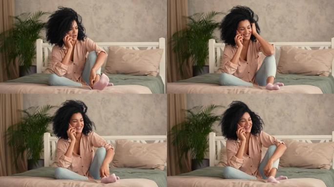 肖像可爱的非洲裔美国女人在智能手机上聊天，开心地微笑。黑人女性坐在卧室里的床上摆姿势，卧室内部明亮。
