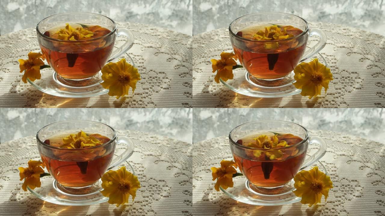 万寿菊的花朵漂浮在冰霜的窗户上的凉茶玻璃杯中