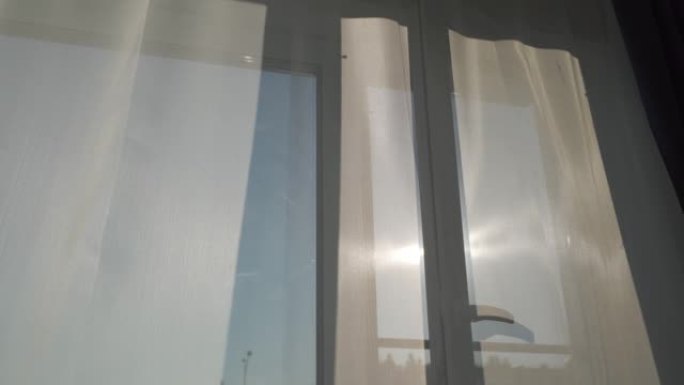 晴天，敞开的窗户上的透明窗帘被风吹动，阳光透过公寓房间窗户上的透明薄纱。