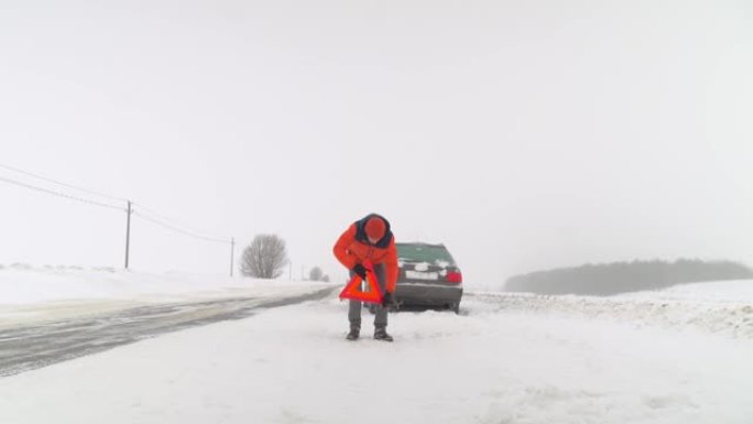 冬天，一名男子在抛锚的汽车旁边设置了紧急停车标志。