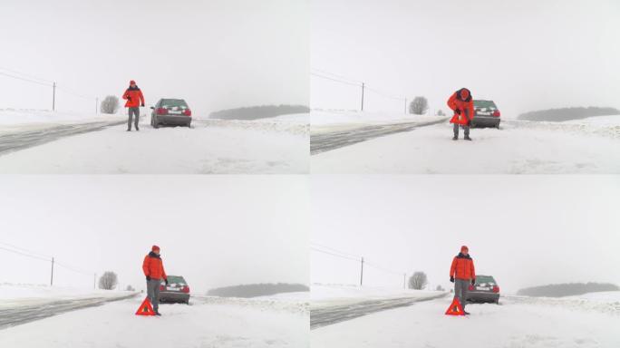 冬天，一名男子在抛锚的汽车旁边设置了紧急停车标志。