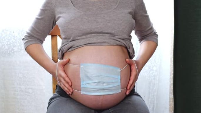 孕妇腹部的特写。未来的母亲在肚子上戴着口罩。新型冠状病毒肺炎，冠状病毒保护。孕妇肚子上戴着防护医用口