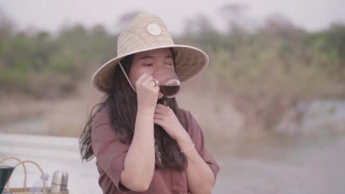 在阳光明媚的日子里，年轻的亚洲妇女在湖边的卡车后面喝咖啡。