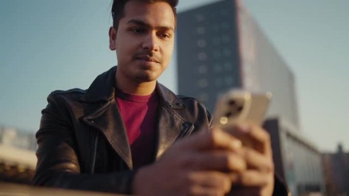 年轻帅气的印度男人在城市里使用智能手机