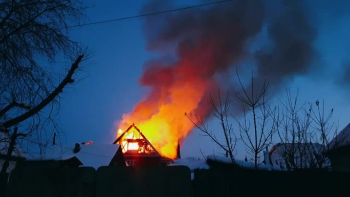 房子的屋顶着火了。居民楼烧毁，村庄。消防员从上方扑灭了起重机上的大火。烟雾和火花。