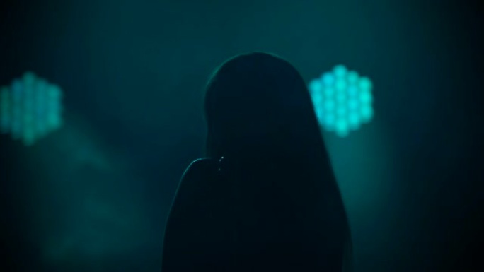 一位女性独奏者在黑色工作室背景上对着复古麦克风唱歌的深色剪影，灯光明亮。这位流行歌星在节日派对上现场