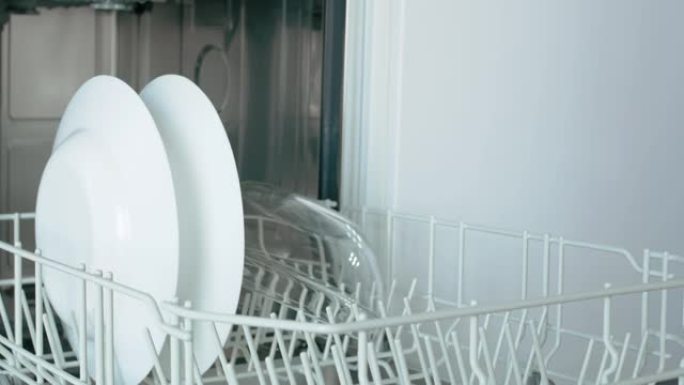 一名妇女从现代洗碗机中拉出抽屉，取出白色汤碗和餐具托盘。特写
