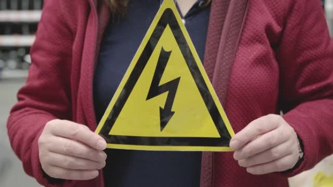 女人拿着黄色的三角形标志，上面画着闪电。高伏特