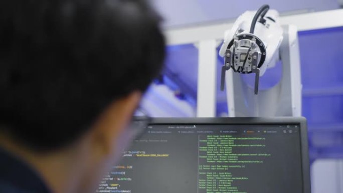 后视图: 机器人手臂有活的生命从年轻的亚洲男子程序员编码到开发自动化生产线机器人手臂应用软件，以提高