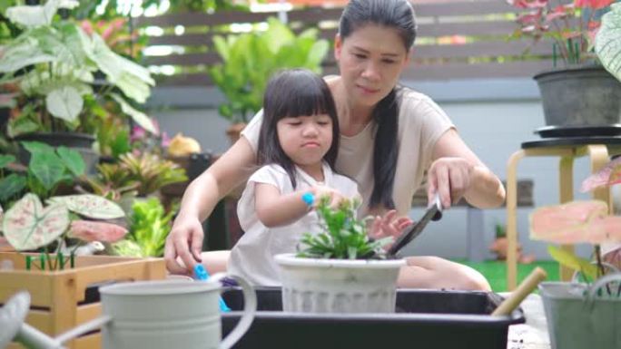 亚洲妇女和她的女儿一起享受时光，在家庭花园里种花。