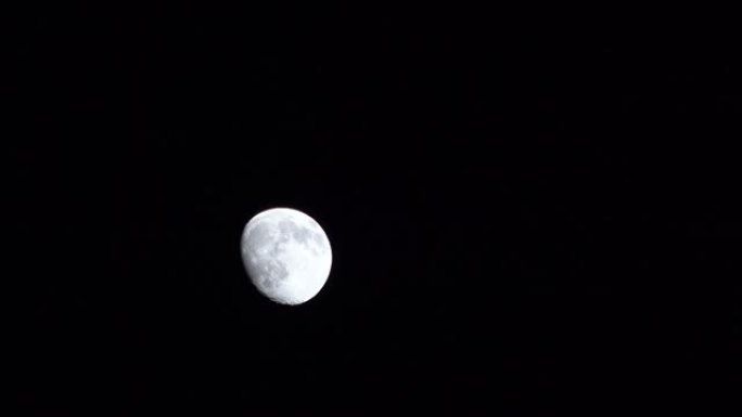 长视频的特写万宁凸灰色月亮从左到右在全黑的天空中移动，出现在左侧，超出摄像机视图水平移动，消失在右侧