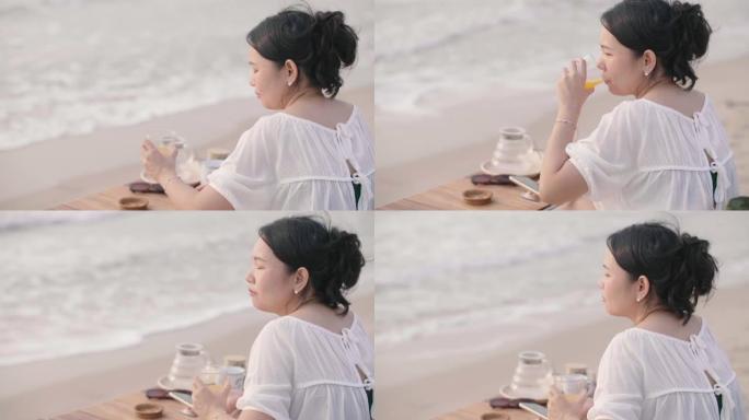 年轻女子在海滩上放松和使用智能手机时喝橙汁。