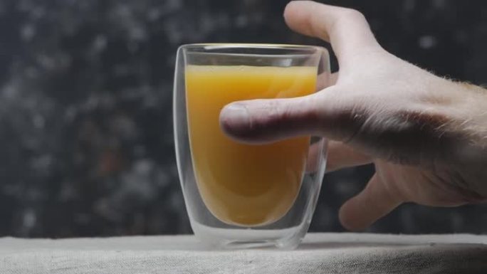 男人的手拿起一杯柑橘汁。特写。黑色背景