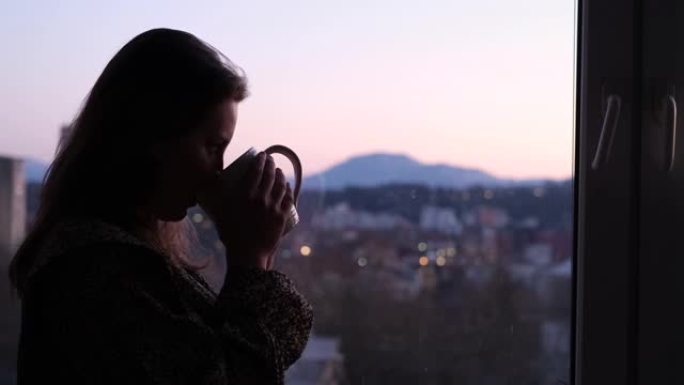有个女人站在窗边，喝着茶，看着日落。