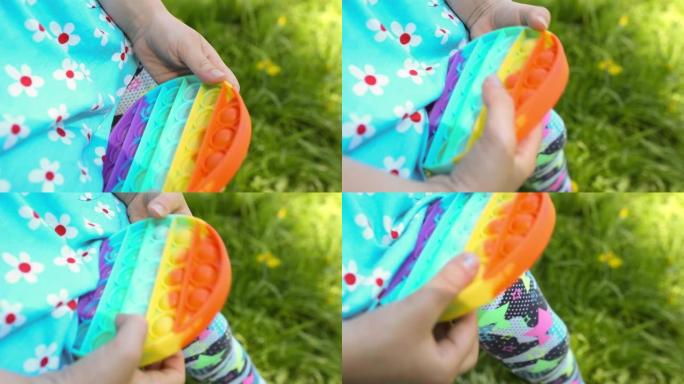 女孩在花园里玩触摸抗压力硅胶流行玩具。手指按下彩虹软气泡和按钮。发展精细运动技能和缓解压力的趋势游戏