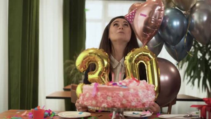 年轻开朗的白人女士坐在家里的桌子旁，庆祝自己的生日。手里拿着两个数字30的气球。网络摄像头的观点。