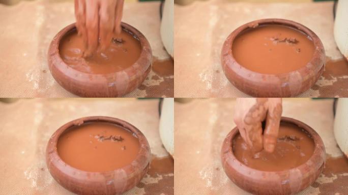 陶工将手浸入水容器中以吸收水分，以与粘土一起工作