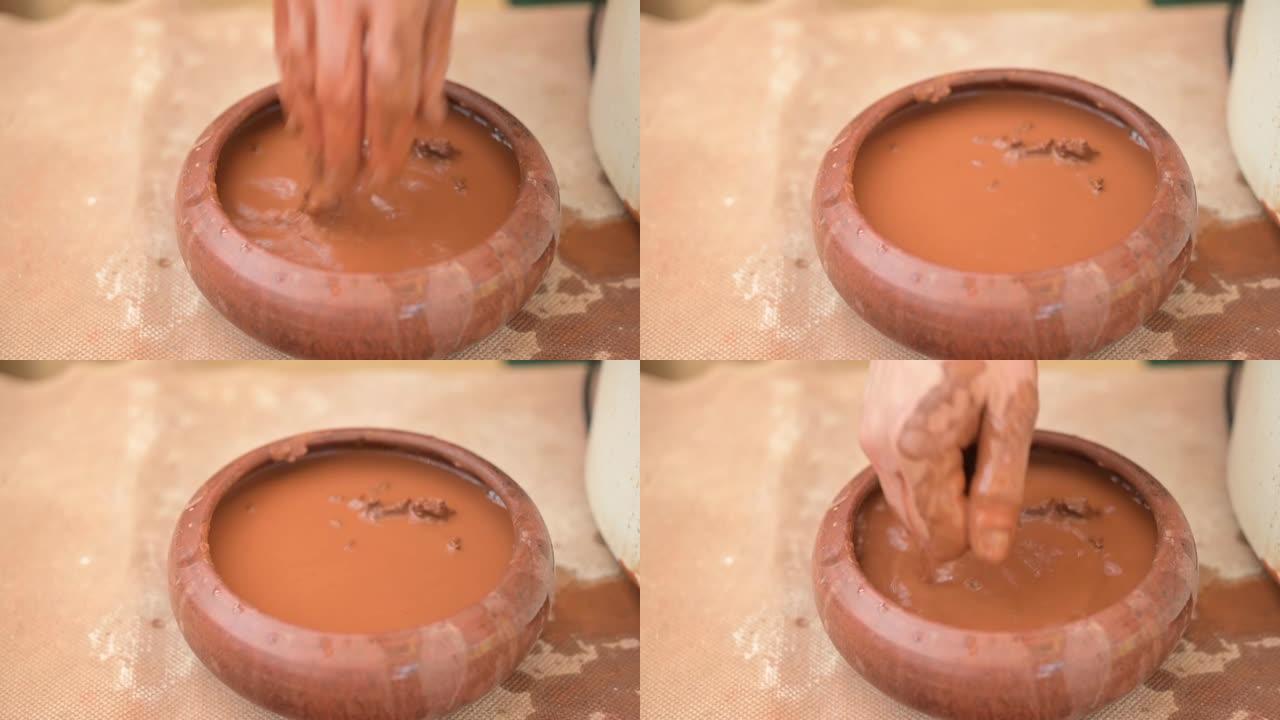 陶工将手浸入水容器中以吸收水分，以与粘土一起工作