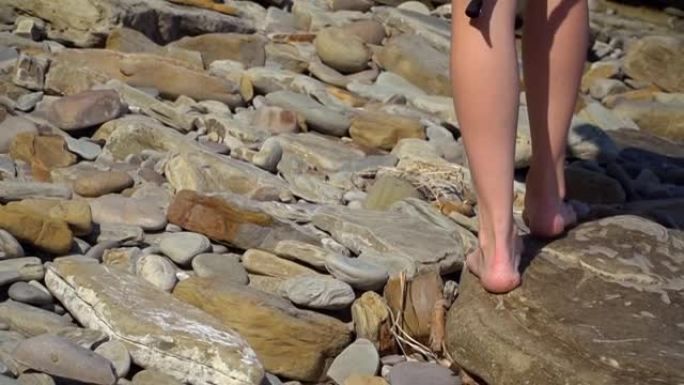女人的腿在石头上行走。一位游客沿着锋利的陡峭石头行走。徒步旅行。女性的腿站在沙滩上的石头上。