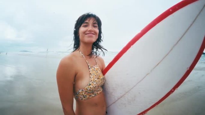 冲浪女孩。穿着比基尼的年轻女子冲浪者站在沙滩上冲浪板上，在阴天摇了摇头。巴西的坎佩切冲浪点