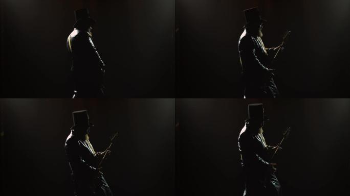 大胡子的摇滚贝斯手在演播室表演中与烟雾和霓虹灯一起独奏。戴着帽子和长长的皮革斗篷的男人的剪影弹吉他。