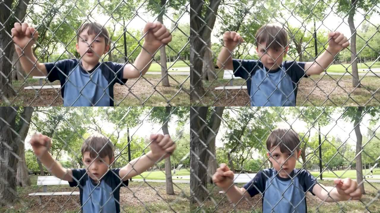 高加索人沉思的小男孩透过校园链条围栏摇晃它