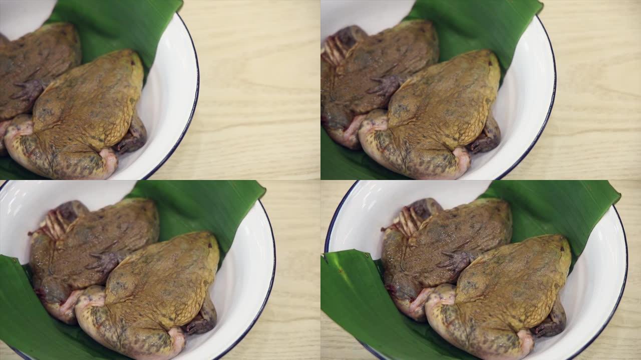 新鲜的生青蛙放在一个带有香蕉叶的白色碗上，一碗新鲜青蛙