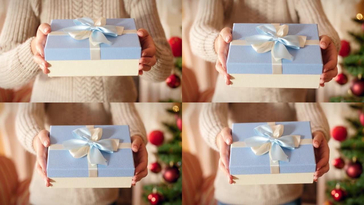 特写4k镜头，年轻女子拿着漂亮的盒子，礼物用丝带和蝴蝶结绑着。家庭在圣诞树旁边的客厅赠送和接收新年礼