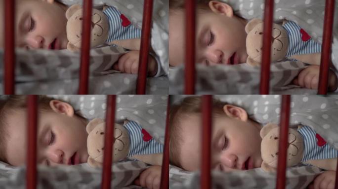 关闭正宗可爱的小婴儿胖乎乎的女婴或男孩在午餐时间甜蜜地睡在卧室和泰迪熊的婴儿床里。孩子躺在灰色的床上