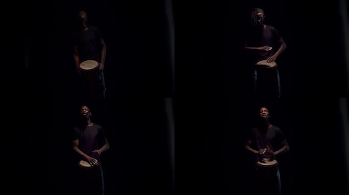 来自黑暗的黑人鼓手微笑着在非洲鼓上演奏。快乐的音乐家打鼓，黑色背景。音乐和艺术的概念