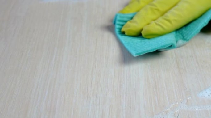 人的手，用蓝色抹布和超细纤维的黄色橡胶手套，用清洁剂小心地清洁桌子上的灰尘和污渍。