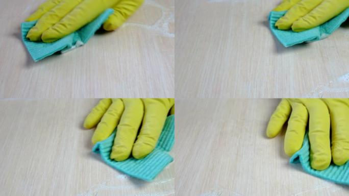 人的手，用蓝色抹布和超细纤维的黄色橡胶手套，用清洁剂小心地清洁桌子上的灰尘和污渍。