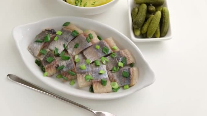 将鲱鱼片与大葱，煮土豆，莳萝和小黄瓜片放在白色盘子上。