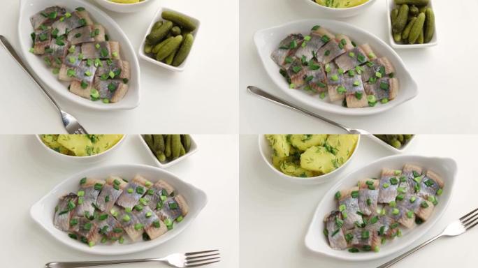 将鲱鱼片与大葱，煮土豆，莳萝和小黄瓜片放在白色盘子上。