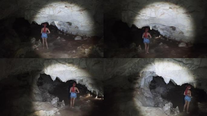 女人在一个深沉的黑暗洞穴中探索钟乳石，用手电筒照亮