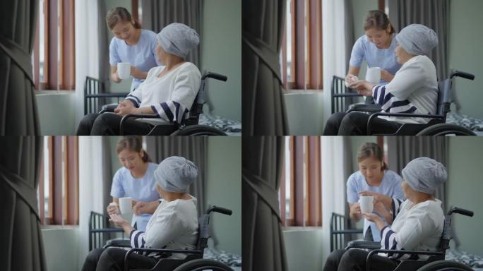 年轻的支持性亚洲女性护理员护士及时帮助患者吃药，而患有癌症的亚洲高级女性坐在轮椅上放松看风景，这个女