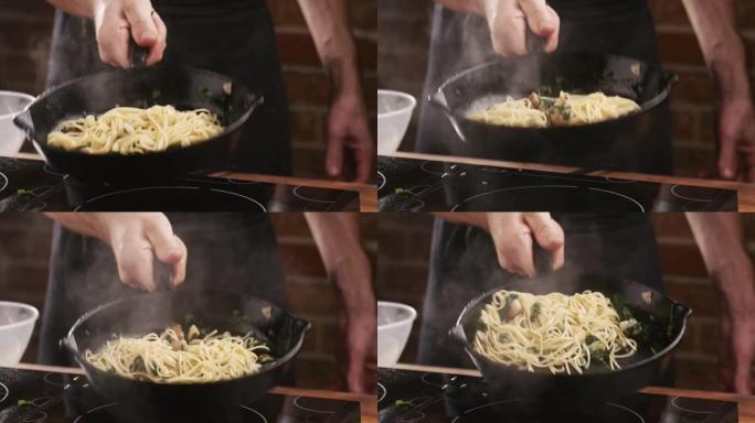 男人在平底锅里混合意大利面，在家庭厨房里用油炸蘑菇、大蒜和欧芹。在家烹饪意大利面食