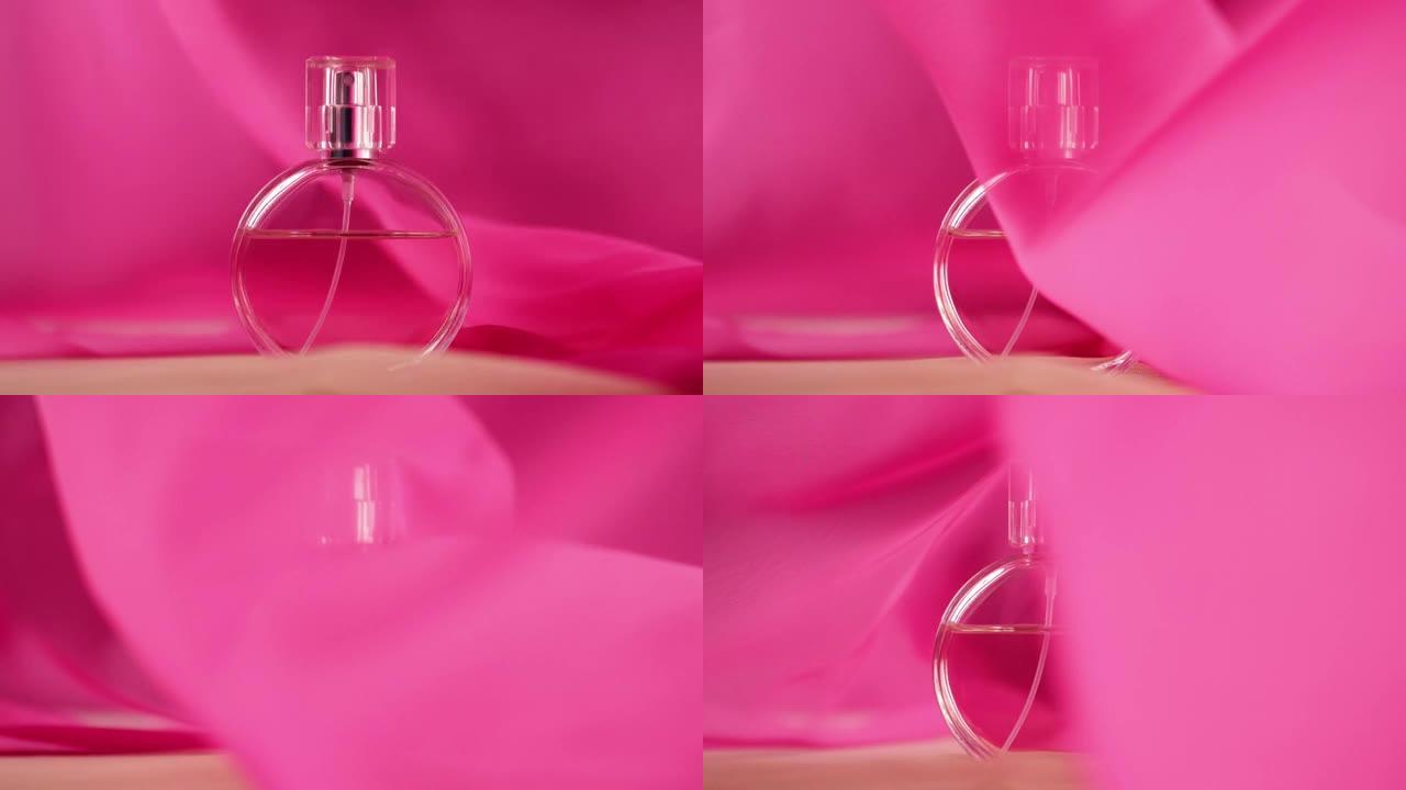 椭圆形的瓶子上有粉红色的香水或精油。粉红色的织物四处飘动，瓶子周围的空气中飘扬。香气和气味的概念。特