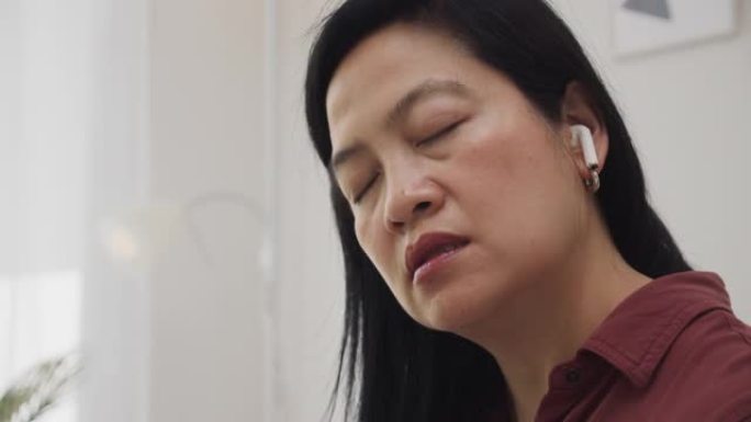 疲倦的亚洲女性倦怠综合症在与团队完成视频电话会议后，女性将头躺在沙发上坐在家里工作