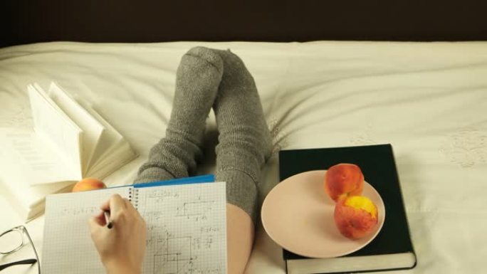 年轻女孩坐在床上，在笔记本上写一个数学方程式，舒适舒适的生活方式。