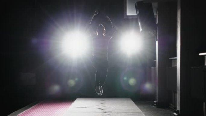 体操女孩的慢动作站在投影仪的灯光下，在健身房翻筋斗。女子运动员体操运动员练习表演艺术体操元素，训练前