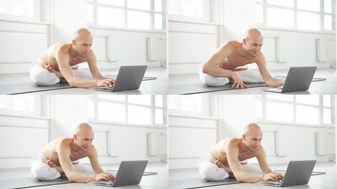年轻的秃头男子将通过在线说明进行复杂的瑜伽姿势