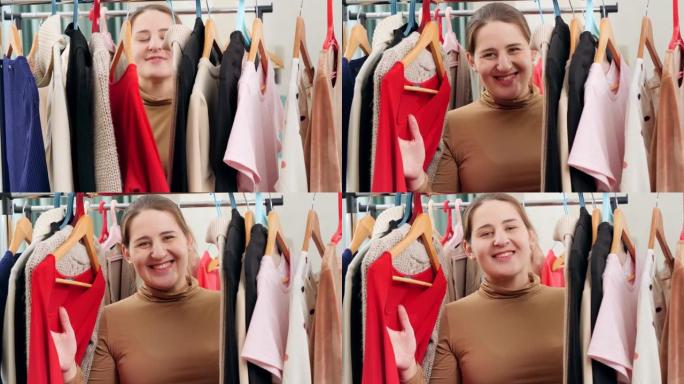 快乐微笑的女人站在衣架之间的大衣柜里，在相机里微笑