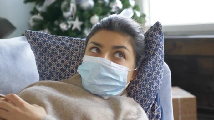 戴着面具的印度不适女性的特写镜头，躺在格子下的房间沙发上，感冒了。年轻漂亮的病人感觉不好。大流行病毒