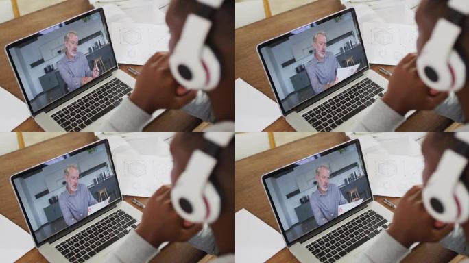 非裔美国商人坐在办公桌前，使用笔记本电脑与男同事进行视频通话