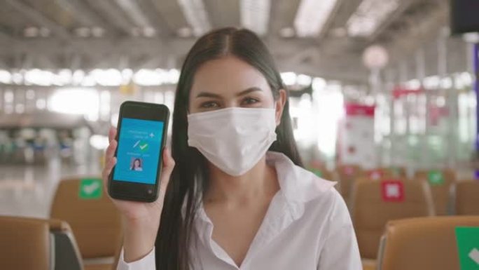 特写一名女商人在国际机场戴着防护口罩，在智能手机上展示疫苗护照，在新型冠状病毒肺炎概念下旅行
