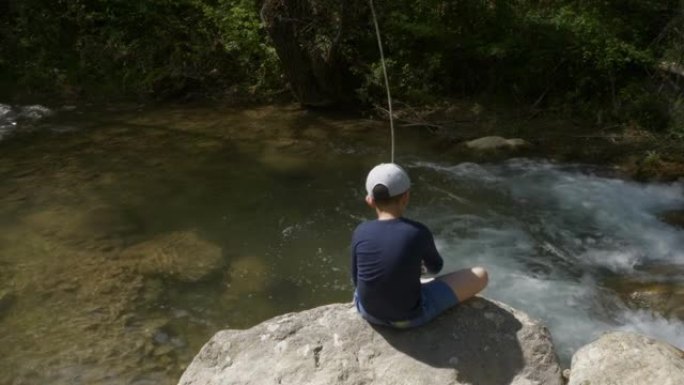 男孩坐在美丽的山溪边的岩石上钓鱼