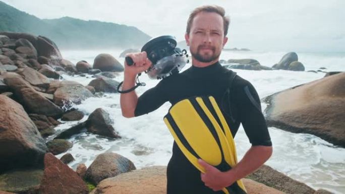 冲浪摄影师。高加索水下摄影师的肖像站在岩石海岸上，有鳍和水下房屋，背景上有海浪
